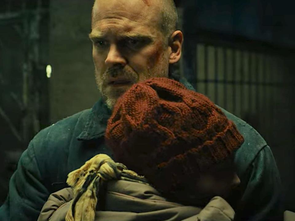 joyce byers hugging hopperin a russian prison, with her back to the camera. hopper has a bewildered, almost overwhelmed expression on his face
