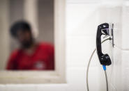 A detainee waits for a visit from family who must communicate through a phone at the Stewart Detention Center, Friday, Nov. 15, 2019, in Lumpkin, Ga. Visitors sit in separate rooms when visiting detainees and no physical contact is permitted. (AP Photo/David Goldman)