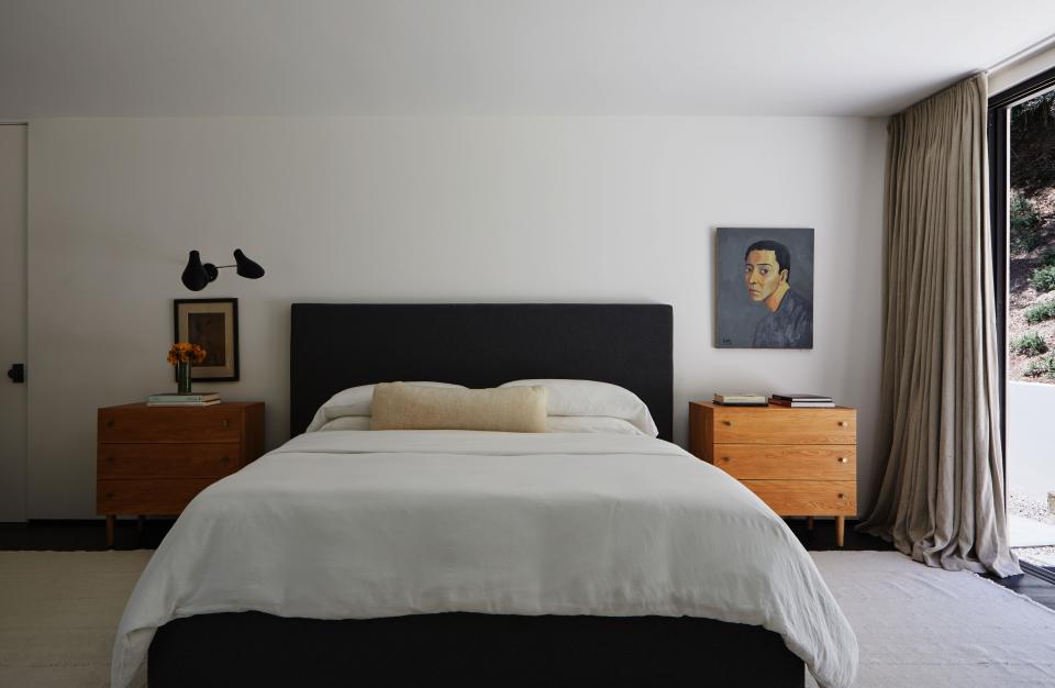 Each side of the custom bed was upholstered in Ralph Lauren cashmere, and the side tables were created with a pair of Milo Baughman chests of drawers from West Coast Modern LA. The white wool kilim rug is from Lawrence of La Brea; the midcentury two-arm sconce is from Stilnovo; and the untitled artwork, a self-portrait, is by Chinese painter Guo Jinyi.