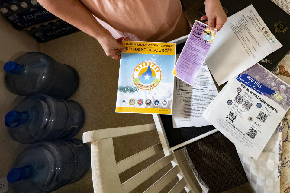 Richelle Dietz holds a couple of brochures containing resources for U.S. military families affected by the on-base housing water contamination from a jet fuel leak in 2021, at her home, Monday, April 22, 2024, in Honolulu, Hawaii. (AP Photo/Mengshin Lin)