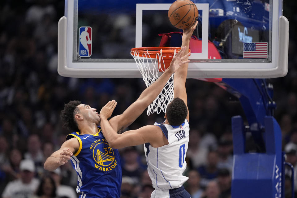 Golden State Warriors' Trayce Jackson-Davis (32) takes a hand to the face from Dallas Mavericks guard Dante Exum (0) as Exum shoots during the first half of an NBA basketball game in Dallas, Wednesday, March 13, 2024. (AP Photo/Tony Gutierrez)