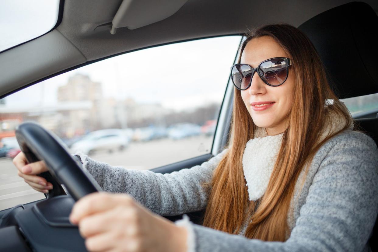 Young woman drive a car in winter. Smiling european woman steering wheel inside a car