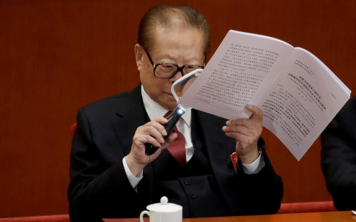 Former Chinese President Jiang Zemin uses a magnifier as he reads Chinese President Xi Jinping's report - REUTERS