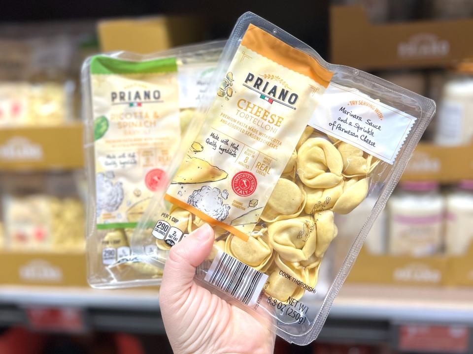 A hand holding two containers of Priano pasta: one ricotta-and-spinach ravioli and one cheese tortelloni.