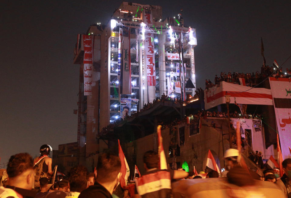 In this Oct. 31, 2019, photo, Iraqi anti-government protesters hang their demands and slogans while standing on a building near Tahrir Square, Baghdad, Iraq. An abandoned building in central Baghdad has emerged as the epicenter of anti-government protests in Iraq, with hundreds holed up inside. The Saddam Hussein-era building known as the “Turkish Restaurant” overlooks Tahrir Square, the Tigris River and the Green Zone, and protesters who took it over on Oct. 25 have sworn not to leave it. (AP Photo/Hadi Mizban)