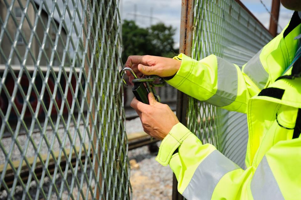 A person in a bright yellow jacket locks a wire fence. 