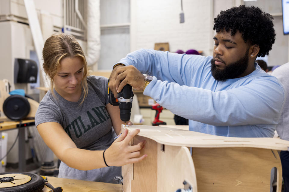 This photo released by Tulane University shows biomedical engineering students Leah Abraham, left, and Shayne Shelton use a drill to secure a side panel of a mobility chair, as they build the specially designed chairs for children at the MakerSpace workshop at the university Sunday, Sept. 24, 2023. The students are making the second batch of mobility chairs for toddlers, that will eventually go to pediatric patients at Children's Hospital. Wheelchairs are expensive, and insurance won't cover the cost for children unless the child proves they can operate it independently. (Sabree Hill/Tulane University via AP)