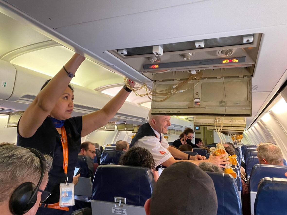 Flight attendants put away oxygen masks that deployed during an Air North flight from Vancouver to Whitehorse on Wednesday. The flight was forced to make an emergency landing in Prince George, B.C. (Wayne Vallevand/CBC - image credit)