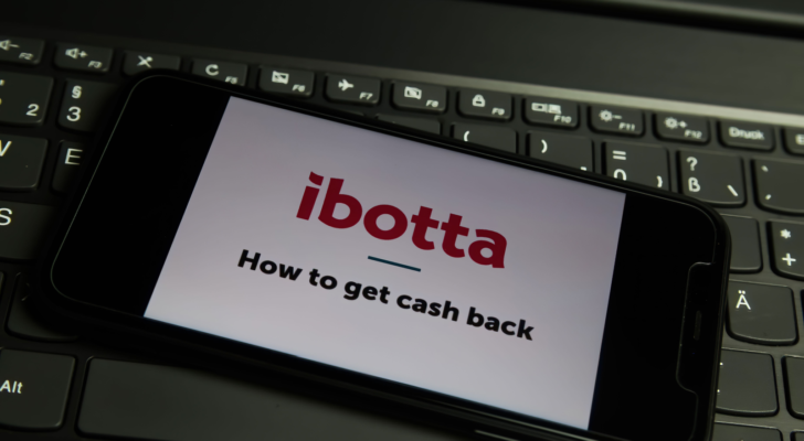 Closeup of mobile phone screen with logo lettering of ibotta (IBTA) cashback app on computer keyboard (focus on left letter t upper lettering)