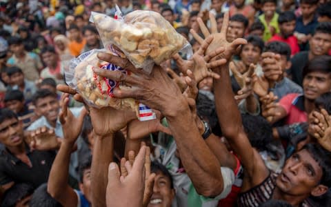 Rohingya Muslims, who crossed over from Myanmar into Bangladesh, stretch their arms out to receive packets of biscuits thrown at them as handouts - Credit: Dar Yasin/AP