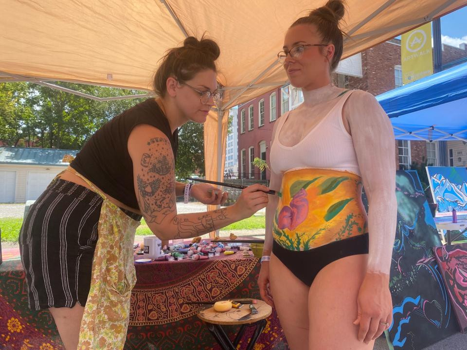 Springfield artist Alicia Mau paints on the body of 
Kristen Smith on Saturday at the MIDXMIDWST mural art and culture festival.