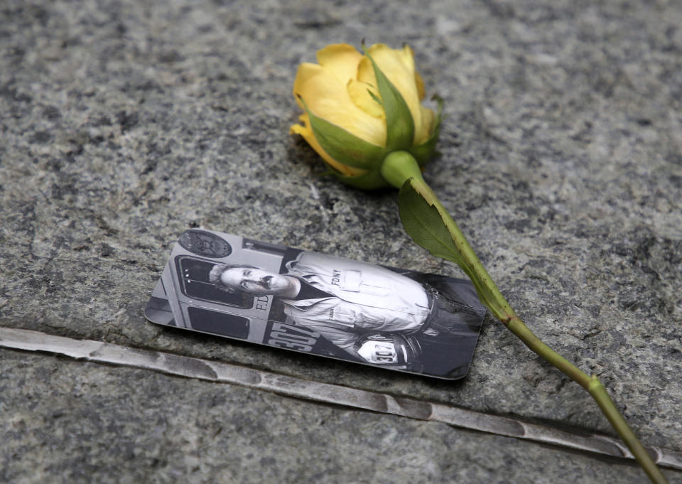 FILE - In this May 30, 2019 file photo, a rose rests next to a photograph of New York City Fire Department Lt. Steven Reisman in the 9/11 Memorial Glade near the National September 11 Memorial & Museum. Reisman searched through the World Trade Center debris for remains, and then died in 2014 of brain cancer at age 54. When the names of nearly 3,000 Sept. 11 victims are read aloud Wednesday, Sept. 11, 2019, at the World Trade Center, a half-dozen stacks of stone will quietly salute an untold number of people who aren’t on the list. (AP Photo/Seth Wenig, File)