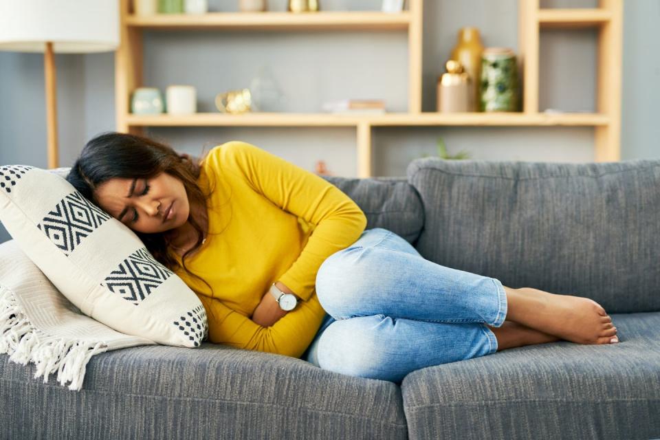 shot of a young woman on the sofa at home holding her stomach in pain