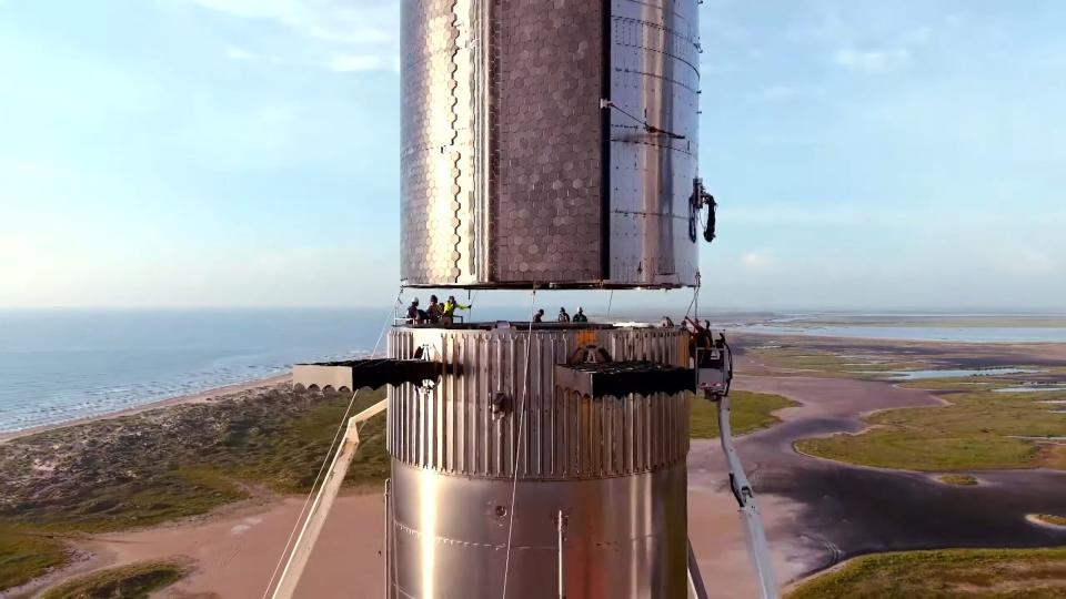 Humans standing in between Starship and Super Heavy Booster before the two are connected.