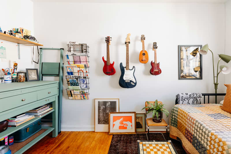 Guitars hang on wall in white room with workspace and daybed.