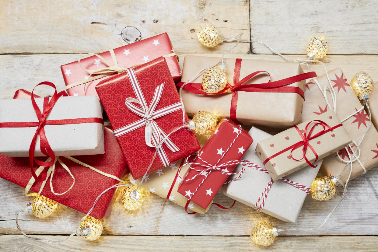 High angle view of a lot of wrapped Christmas gifts and strings lights on wooden background