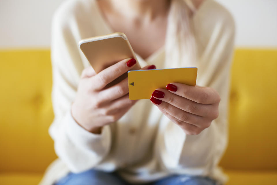 A woman is sitting and holding a phone in her right hand and a credit card in her left hand.