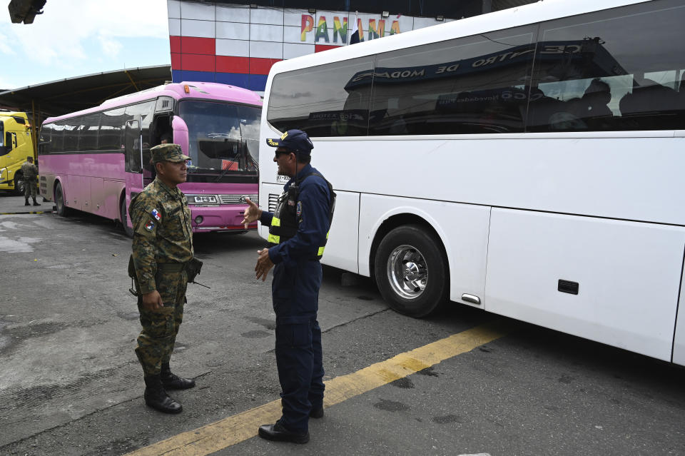 A Panamanian police officer, left, speaks with a Costa Rican migration officer as buses with migrants, mostly from Venezuela, cross the borderline between both countries in Paso Canoas, Costa Rica, Monday, Oct. 16, 2023. Panama and Costa Rica launched a plan to quickly bus thousands of migrants through Panama to the Costa Rican border, as the countries continue to grapple with the increasing number of migrants. (AP Photo/Carlos Gonzalez)