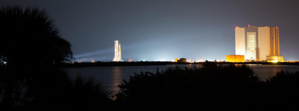 wide shot shows distant rocket rolling far from its assembly building