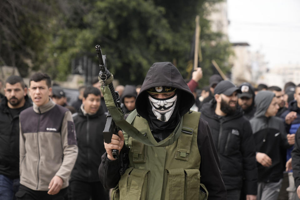 A masked gunman marches alongside of the bodies of Said Jaradat and Yasser Hanoun, both draped in the flag of the Islamic Jihad militant group, on Friday, Feb. 23, 2024. The pair were killed in an Israeli drone strike on a car in the West Bank Jenin refugee camp a day earlier. The Israeli military alleged that Hanoun was previously involved in several shooting attacks targeting Israeli settlements and army posts. (AP Photo/Majdi Mohammed)