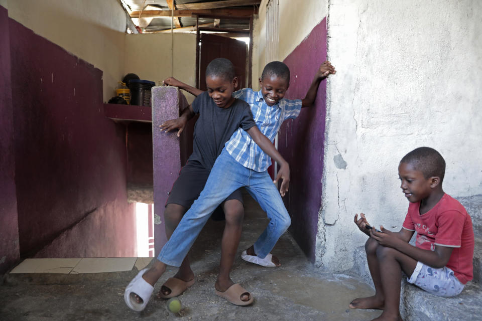 Woodberson Seide, standing right, plays with his little brother Jean Roods Seide as their cousin Belle Fleur Sanshaly sits by at the church where they live in the Delmas 32 neighborhood of Port-au-Prince, Haiti, Saturday, Sept. 23, 2023. Woodberson Seide's family sleeps on the floor of a church, something they've done since losing their home to gangs. (AP Photo/Odelyn Joseph)