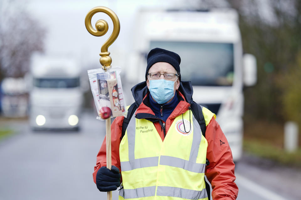 Pastor Michael Ohlemueller is standing at the motorway service station Wonnegau near Worms, Germany, with a crosier with chocolate Santa Claus and apple in a bag, which he wants to distribute as a gift to truck drivers. The action is intended as a thank you and appreciation for the drivers' work. ( Uwe Anspach/dpa via AP)