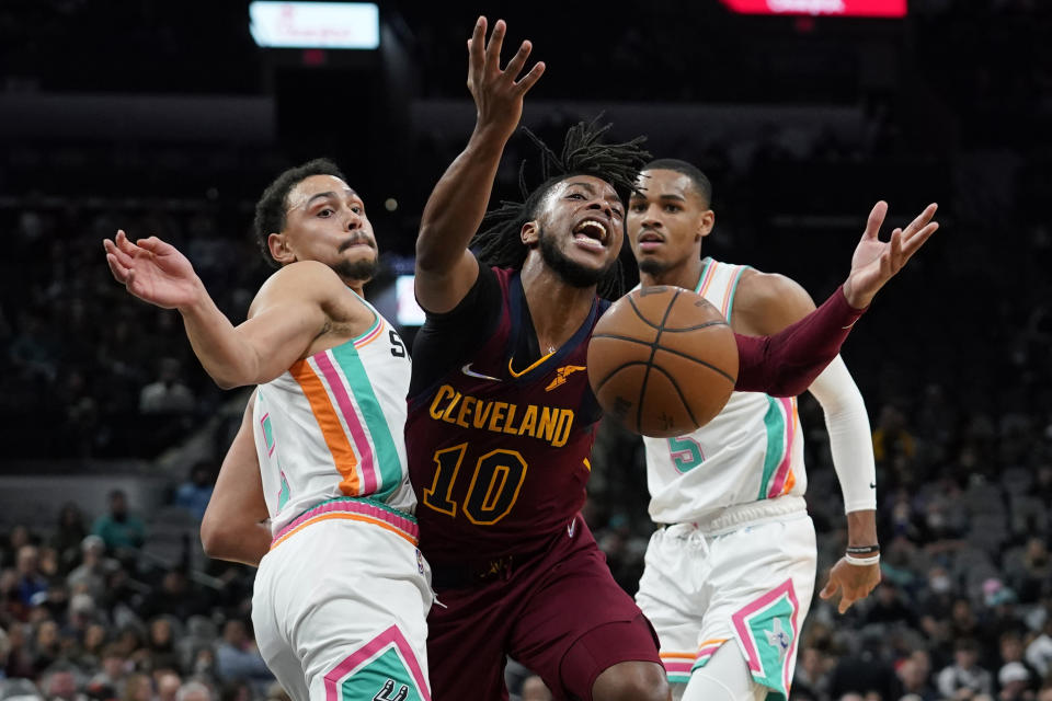 Cleveland Cavaliers guard Darius Garland (10) is fouled as he drives between San Antonio Spurs guards Bryn Forbes, left, and Dejounte Murray (5) during the first half of an NBA basketball game, Friday, Jan. 14, 2022, in San Antonio. (AP Photo/Eric Gay)