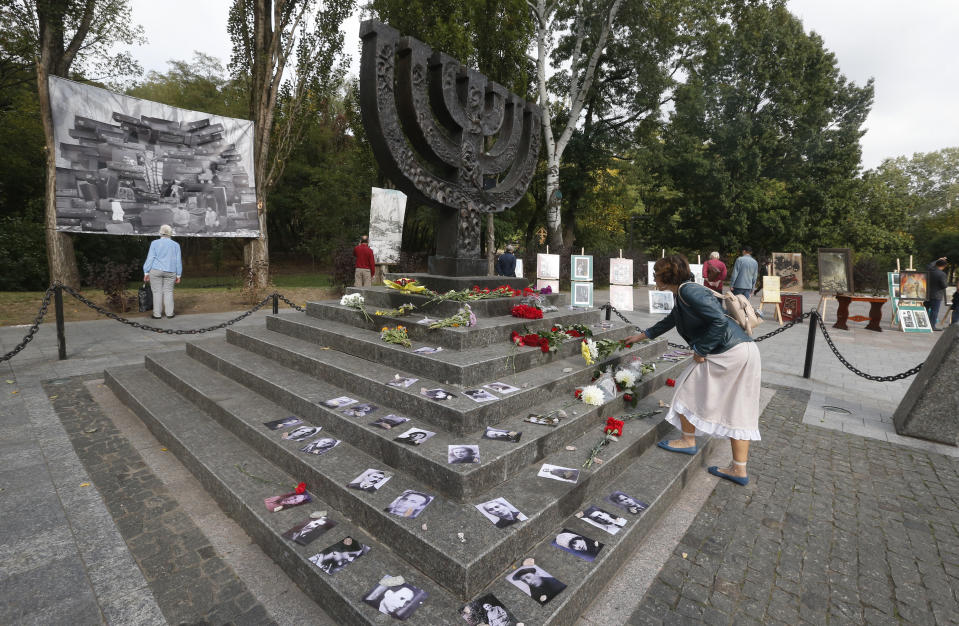 A woman lays flowers at a menorah monument close to a Babi Yar ravine where tens of thousands of Jews were killed during WWII, in Kyiv, Ukraine, Tuesday, Sept. 29, 2020. Photos of victims are seen around the monument. Ukraine marked the 79th anniversary of the 1941 Babi Yar massacre. (AP Photo/Efrem Lukatsky)