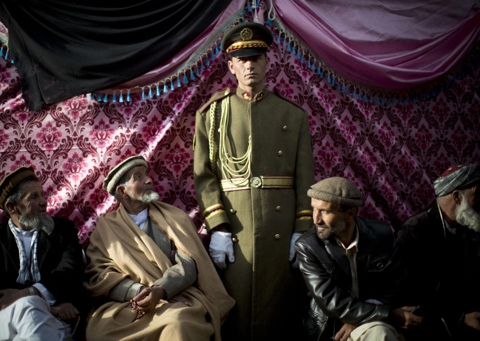 FILE - An honor guard stands next to men who arrived to mourn the death of late Vice President Field Marshal Mohammed Qasim Fahim outside his house in Kabul, Afghanistan, Monday, March 10, 2014. The influential vice president, a leading commander in the alliance that fought the Taliban who was later accused with other warlords of targeting civilian areas during the country's civil war, died March 9, 2014. He was 57. (AP Photo/Anja Niedringhaus, File)