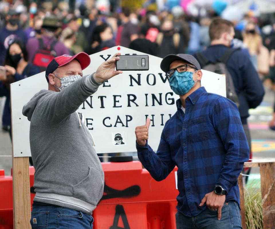 Two man take a picture in front of the Free Cap Hill sign in Seattle during a temporary occupation of what has become known as the Capitol Hill Autonomous Zone.