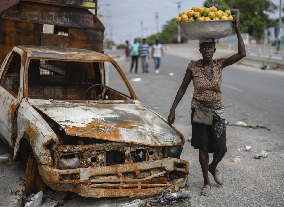 A fruit vendor walks by a burned car in the Delmas district of Port-au-Prince, Haiti, Thursday, May 2, 2024. (AP Photo/Ramon Espinosa)