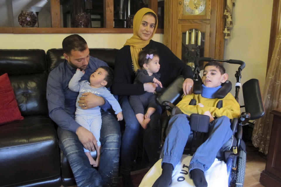 In this Oct. 7, 2019 photo, the Hamideh family poses for a photo inside their home in Blasdell, NY. Parents Ooroba Hamideh, holding daughter Aya Hamideh, and Ali Hamideh, holding son Abdallah Hamideh, say their son Ameer Hamideh, who has cerebral palsy, a seizure disorder and uses a wheelchair, was unfairly removed from school after the district rejected his medical exemption for vaccines. New York has tightened the criteria for medical exemptions after doing away altogether with religious exemptions. (AP Photo/Carolyn Thompson)