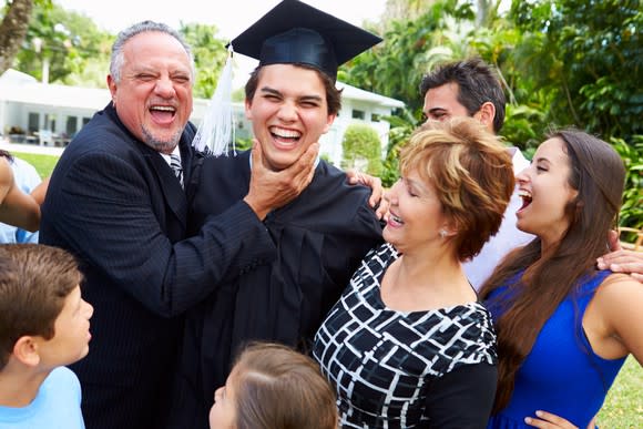 Smiling family gathered outdoors around a graduate in cap and gown.