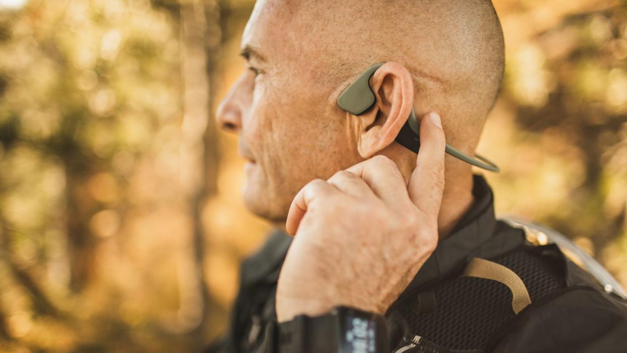 senior man wearing bone conduction headphones to listen music on forest walk or hike close up