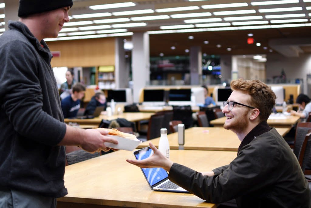 A college student delivers good to another college student in the library. 