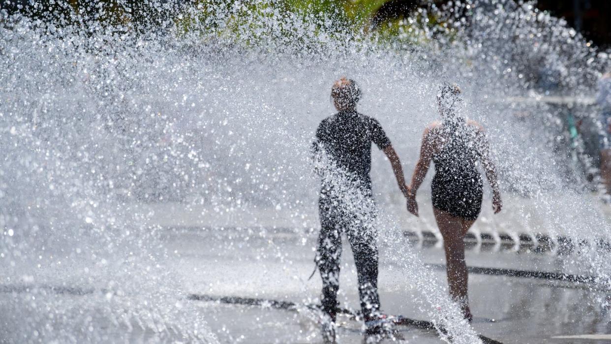 Zwei Jugendliche kühlen sich an einem Springbrunnen am Karlsplatz (Stachus) in München ab.