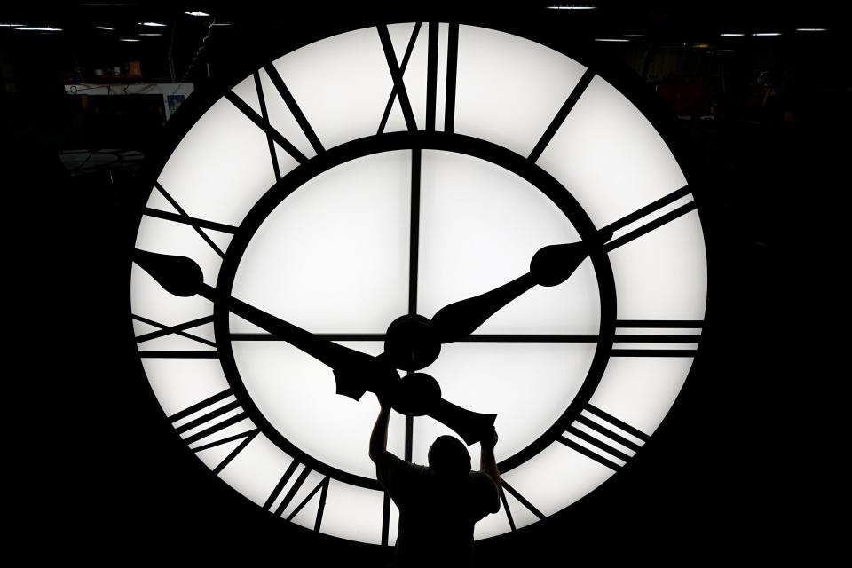 In this March 9, 2021 file photo, Electric Time technician Dan LaMoore puts a clock hand onto a 1000-pound, 12-foot clock constructed in Medfield, Massachusetts, for a resort in Vietnam.