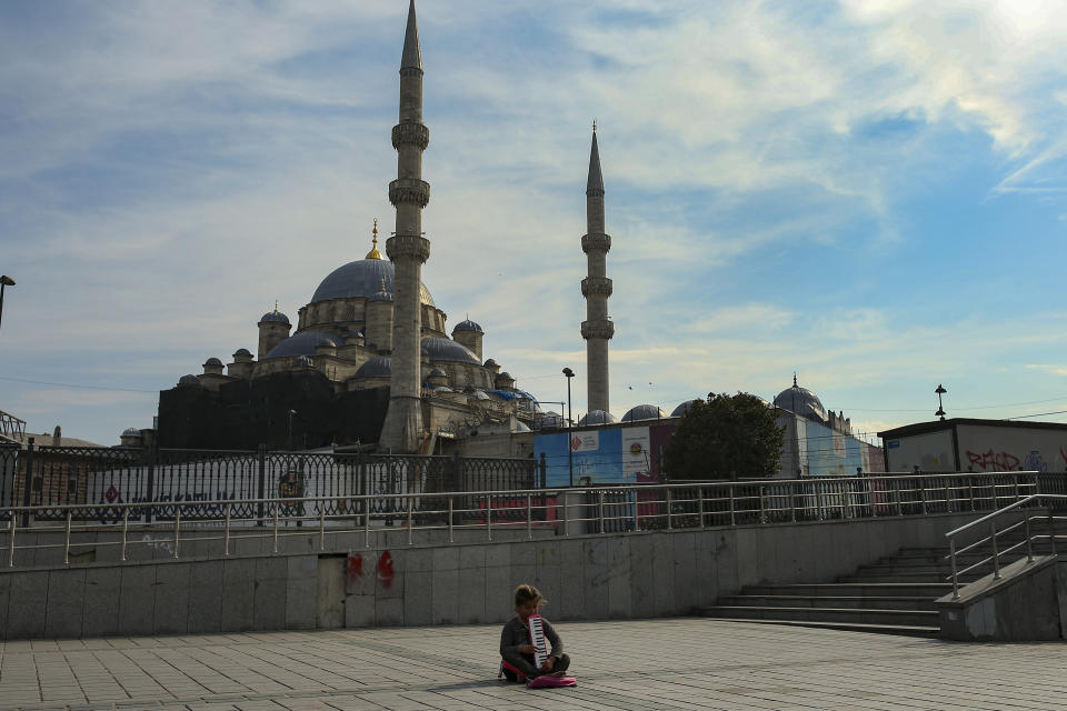 A child plays music for money backdropped by the Yeni Cami (New Mosque) in Istanbul, Saturday, April 3, 2021. The streets of Istanbul, reflect a weekend curfew resumed as the number of COVID-19 cases hit record levels, and with renewed restrictions announced for the Islamic month of Ramadan which begins on April 13. (AP Photo/Emrah Gurel)