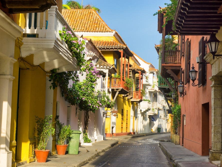 A street lined with colorful houses with balconies. There are lots of flowers and plants.