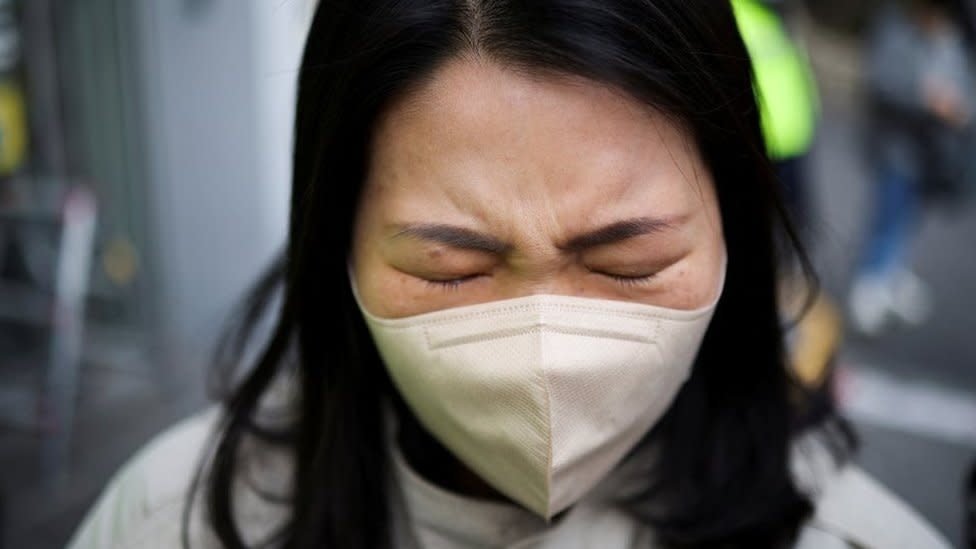 Una mujer con mascarilla llorando con los ojos cerrados