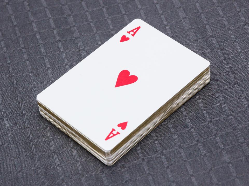 Deck of cards with a red ace of hearts on top on a gray surface