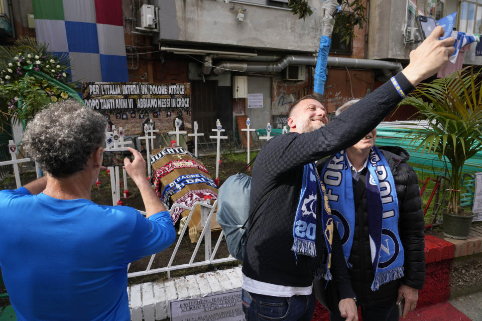 Napoli fans take pictures near a mock cemetery with crosses bearing the Italian Serie A soccer teams flags and a coffin with the scarfs of the Juventus, Milan and Inter teams and a banner in background reading: " for all of Italy an atrocious pain, after so many years we have put you all on the crosses" , is seen in Naples, Italy, Sunday, April 30, 2023. After Napoli's game was moved to Sunday, the team could secure the title in front of their own fans by beating Salernitana — if Lazio fails to win at Inter Milan earlier in the day. Diego Maradona led Napoli to its only previous Serie A titles in 1987 and 1990. (AP Photo/Gregorio Borgia)