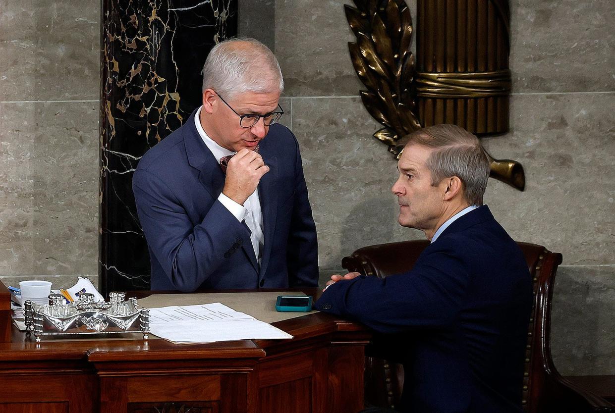 McHenry, standing on the speaker's dais, talks with Jordan, who is staring into the distance to his left.