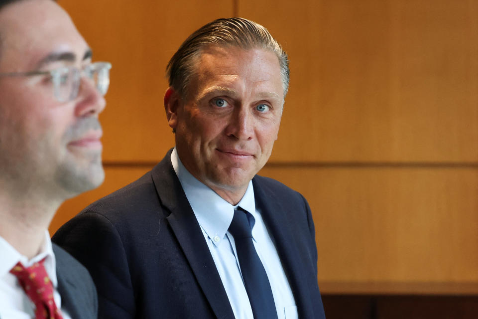 Devon Archer, in suit and tie, accompanied by another man in a corridor.