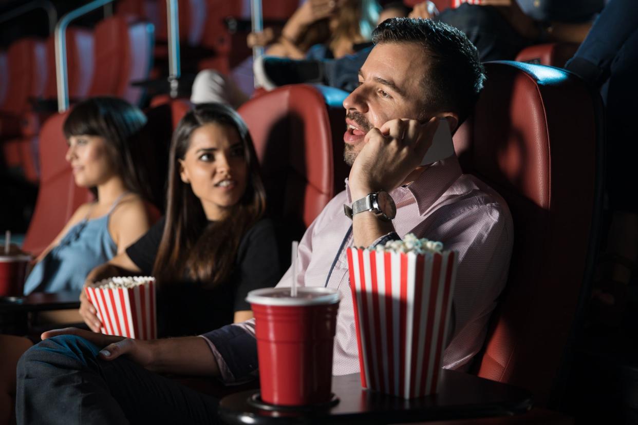 Profile view of a very obnoxious and disrespectful man talking on the phone while sitting in a movie theater