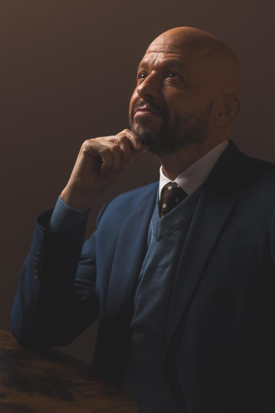 Jon Cryer, in a blue suit, his chin resting on one hand.