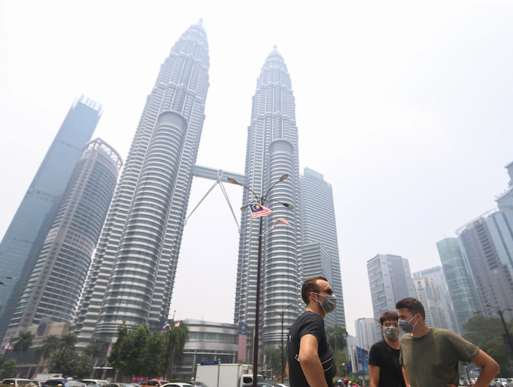 Tourists wear masks as they walk past the Petronas Twin Towers shrouded in haze in Kuala Lumpur September 12, 2019. — Picture by Firdaus Latif