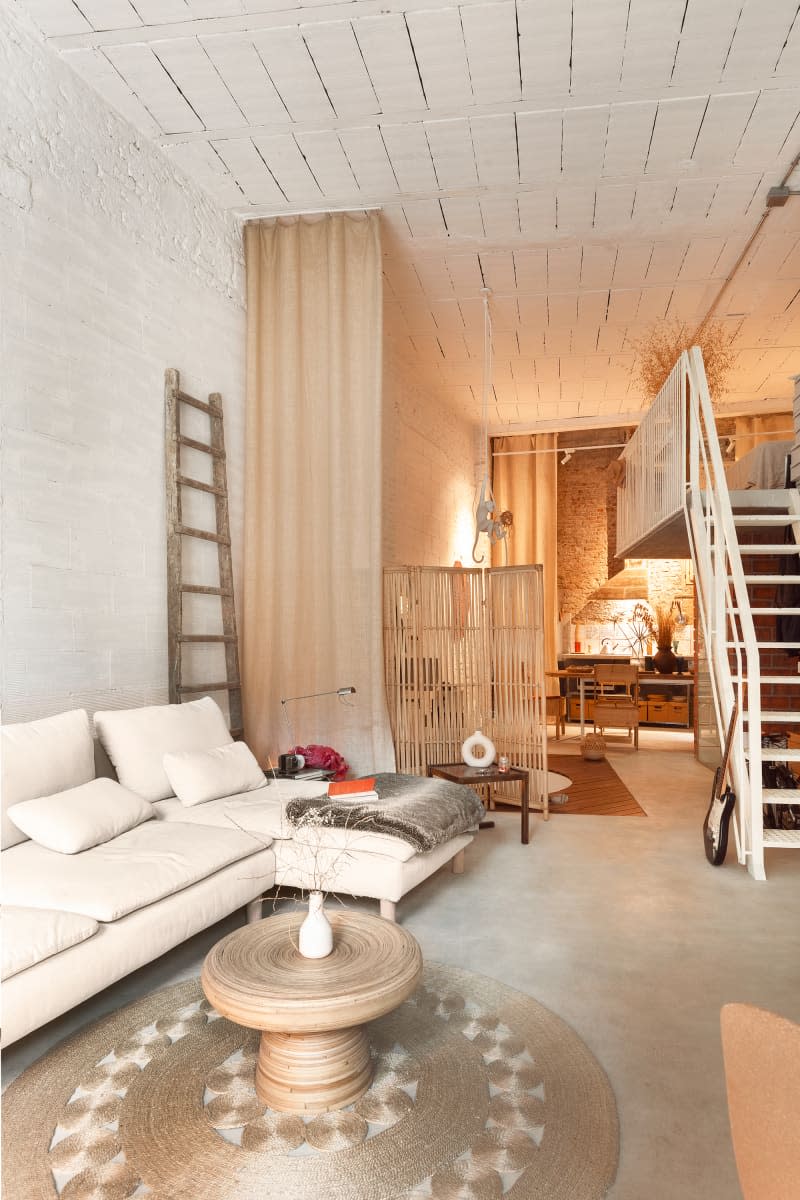 White brick living room with off white sofa, stone floor, large windows, and lots of neutral and warm tones