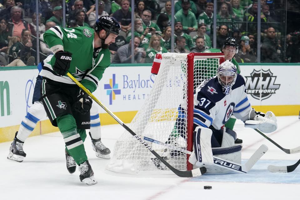 Dallas Stars left wing Jamie Benn (14) makes a pass to the front of the net as Winnipeg Jets goaltender Connor Hellebuyck (37) defends in the first period of a NHL hockey game in Dallas, Monday, Oct. 17, 2022. (AP Photo/Tony Gutierrez)