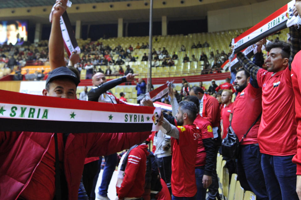 Syrian basketball fans hold their national flags as they cheer during the FIBA Basketball World Cup 2023 Asian Qualifiers Group D match between Syria and Kazakhstan, in Damascus, Syria, Monday, Nov. 29, 2021. Syria hosted the first international athletic tournament on its soil in at least two decades Monday, bringing an Asia region World Cup qualifying game to a packed stadium in the capital Damascus. The game with Kazakhstan, which Syria lost 81-71, saw the national team play at home before fans for the first time since the civil war in Syria disrupted security and upended regular life in the country. (AP Photo/Omar Sanadiki)